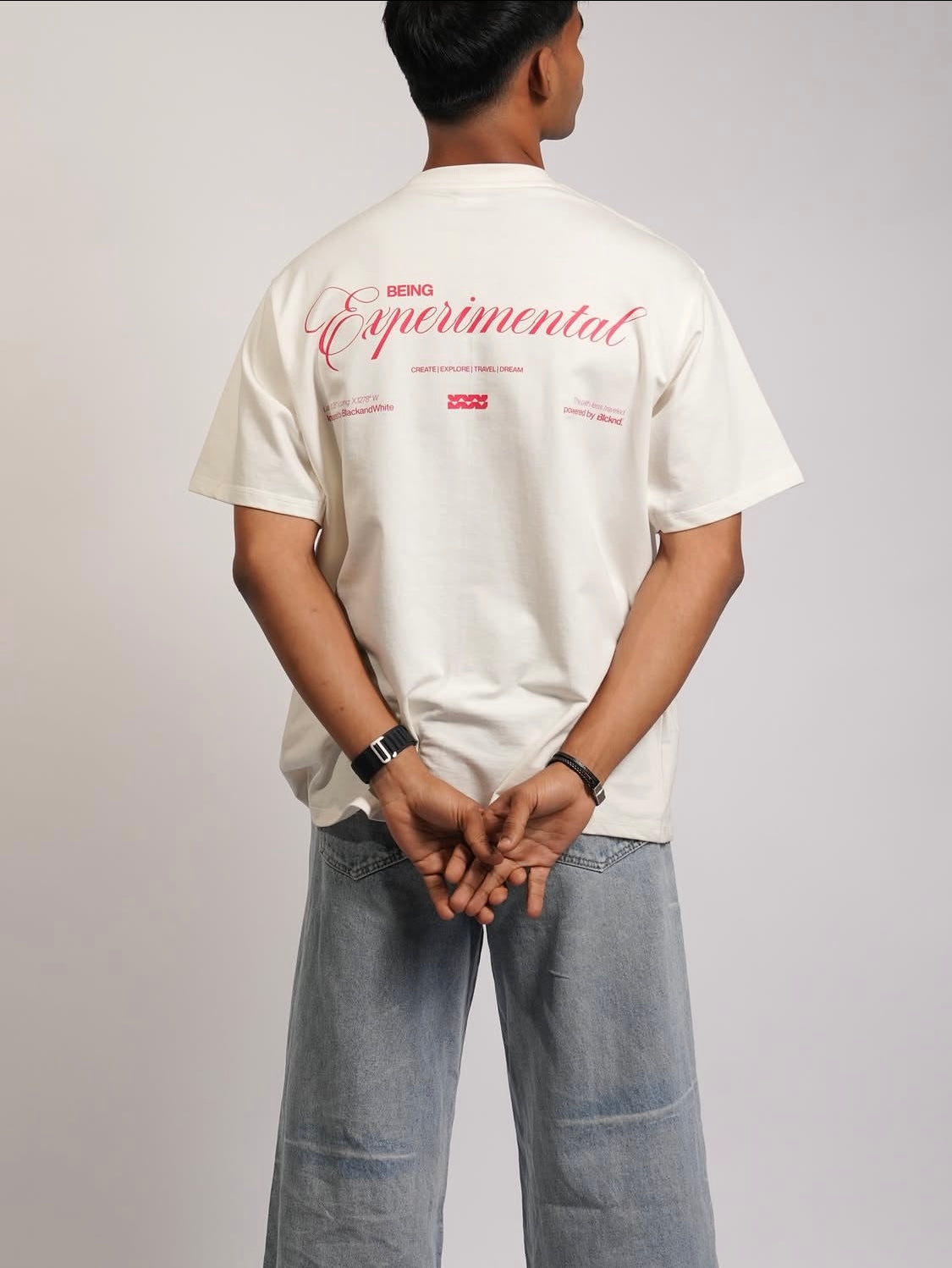 Person wearing a white t-shirt with text on the back, standing against a plain background